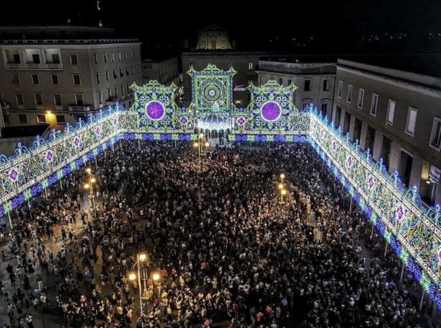 People crowd in front of a large building for the Festa di Sant'Oronzo in Italy, enjoying the festive atmosphere.