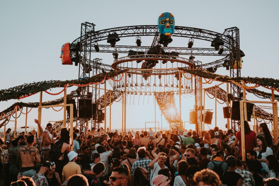Outdoor festival crowd enjoying music at sunset with vibrant decorations and energetic atmosphere.
