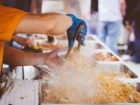 Vendor serving steaming noodles at a vibrant festival food stall.