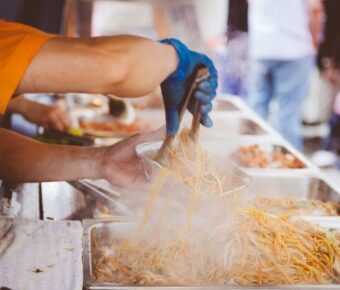 Vendor serving steaming noodles at a vibrant festival food stall.