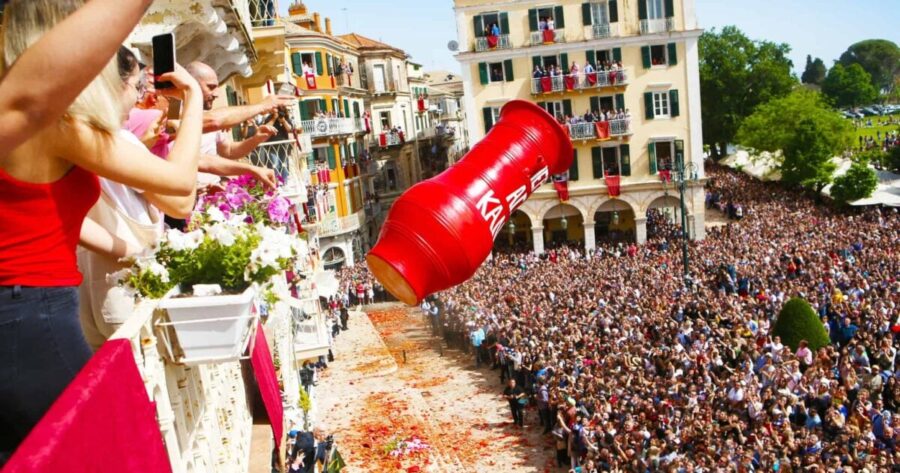 Festive crowd celebrates with red container toss at urban event.