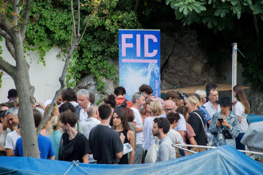Outdoor FIDMarseille event with diverse crowd, vibrant banner, and lush greenery backdrop.