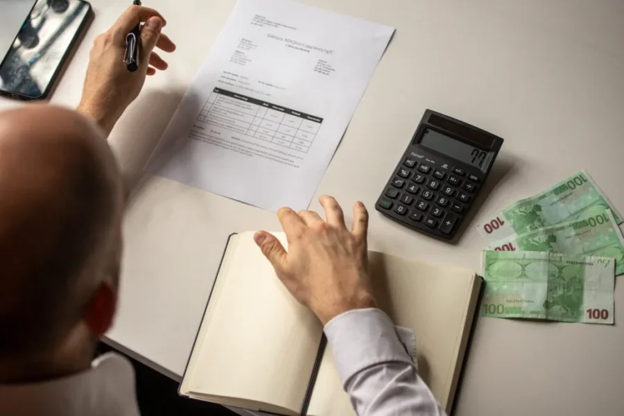 Analyzing financial documents with calculator, smartphone, and cash at a well-lit desk.