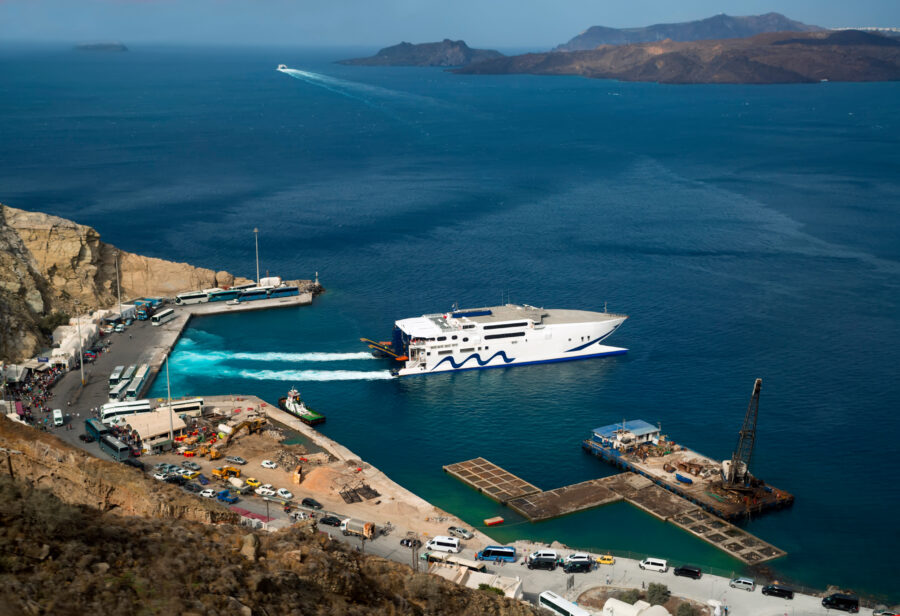Ferry approaching Fira, Santorini, Greece, with white buildings and blue domes visible on the hillside