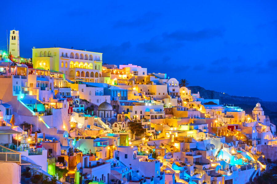 Night view of Fira, Santorini, showcasing illuminated buildings and the Aegean Sea under a starry sky