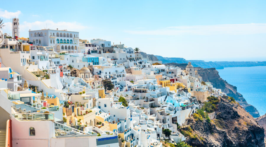 Panoramic view of Fira, Santorini, showcasing white buildings and blue domes against a clear daytime sky