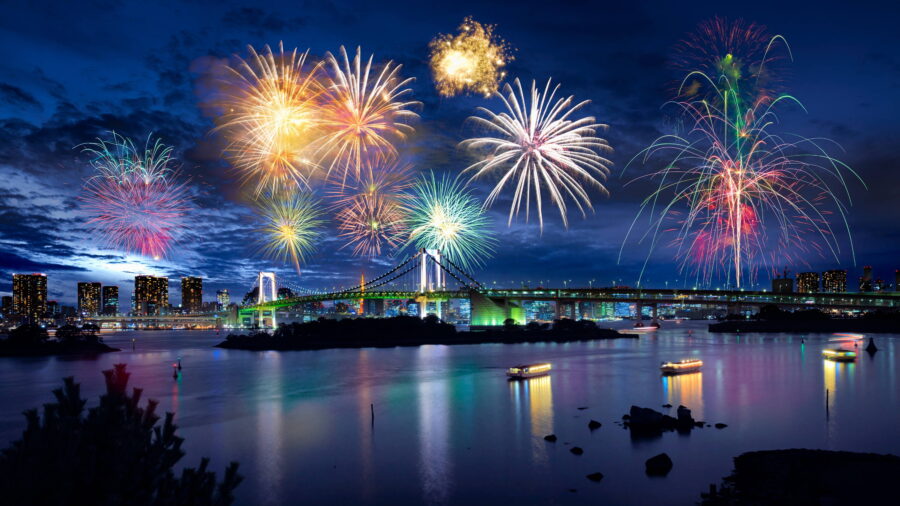 Fireworks illuminate water and cityscape, showcasing a vibrant celebration at night.