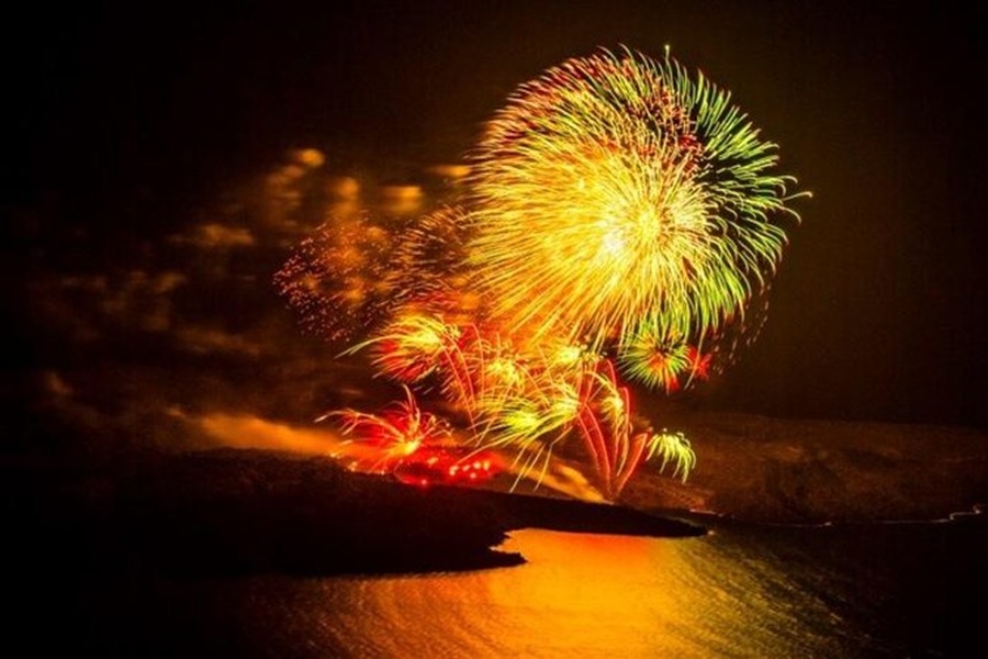 Fireworks illuminating night sky over water at coastline festival celebration.