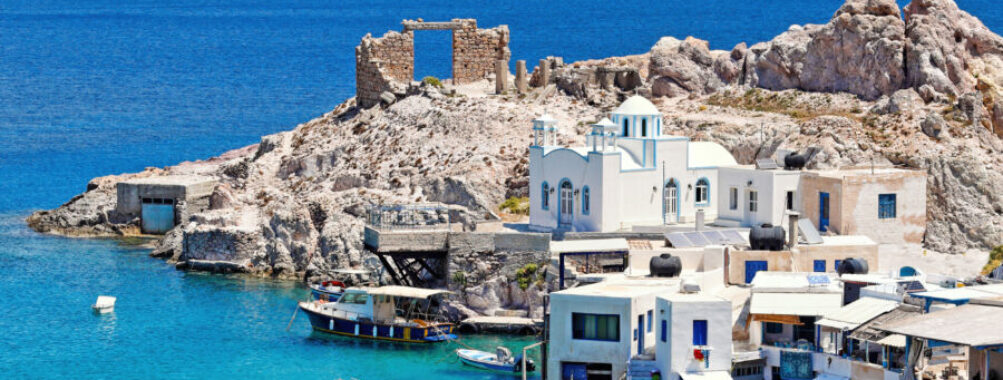 Coastal village of Firopotamos, Milos, featuring a blue-domed church, white houses, and rocky cliffs by the clear sea.