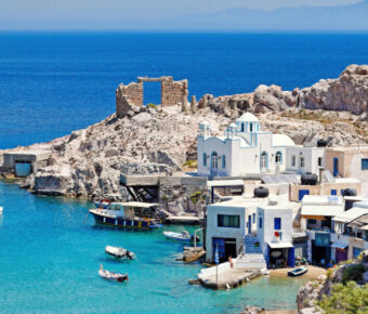 Coastal village of Firopotamos, Milos, featuring a blue-domed church, white houses, and rocky cliffs by the clear sea.