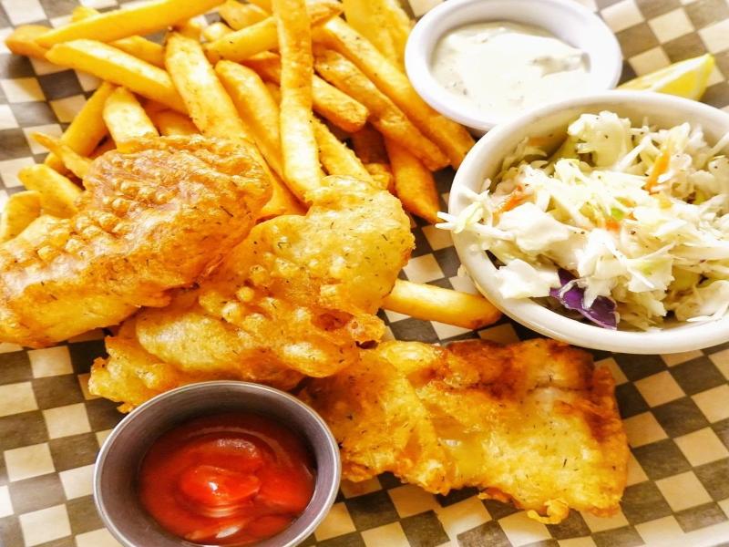 Crispy battered fish and chips with fries, tartar sauce, ketchup, and coleslaw.