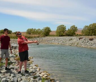 Two people fishing on a sunny riverbank