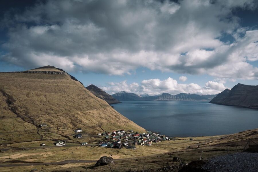 Scenic Faroe Islands village with colorful houses, fjord, green hills, and majestic mountains.