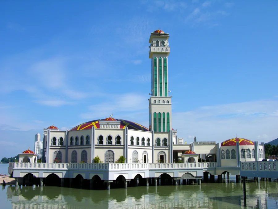 Modern floating mosque on calm water with colorful domes and tall minaret under clear sky.