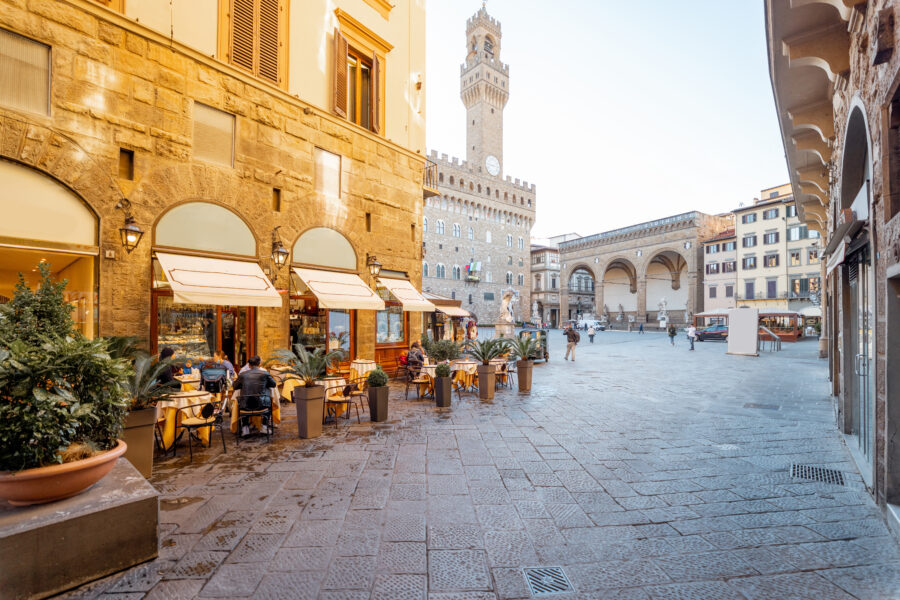 Charming restaurant terrace in Florence, Italy, with a view of the Vecchio Palace tower near a bustling central square
