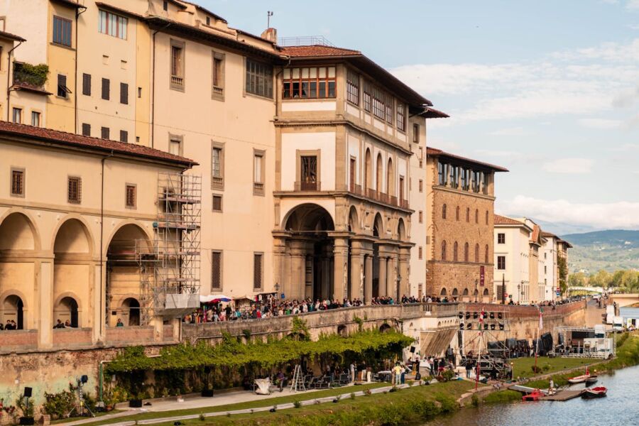 Riverbank scene in Florence with historic architecture, tourists, and event preparations.
