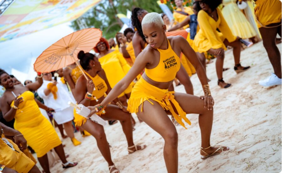 Lively group of women dressed in yellow dances on the beach, celebrating the Food and Rum Festival in Barbados.