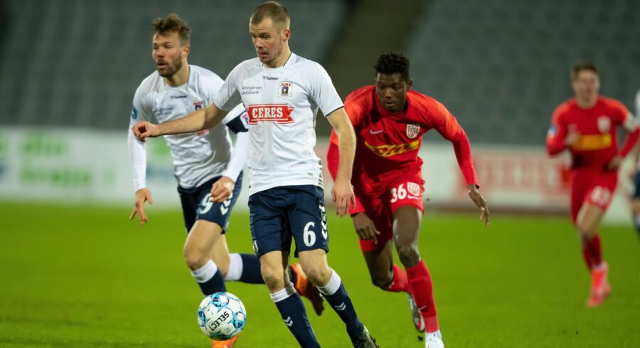 AGF Aarhus number 6 dribbling soccer ball under pressure from red opponent.