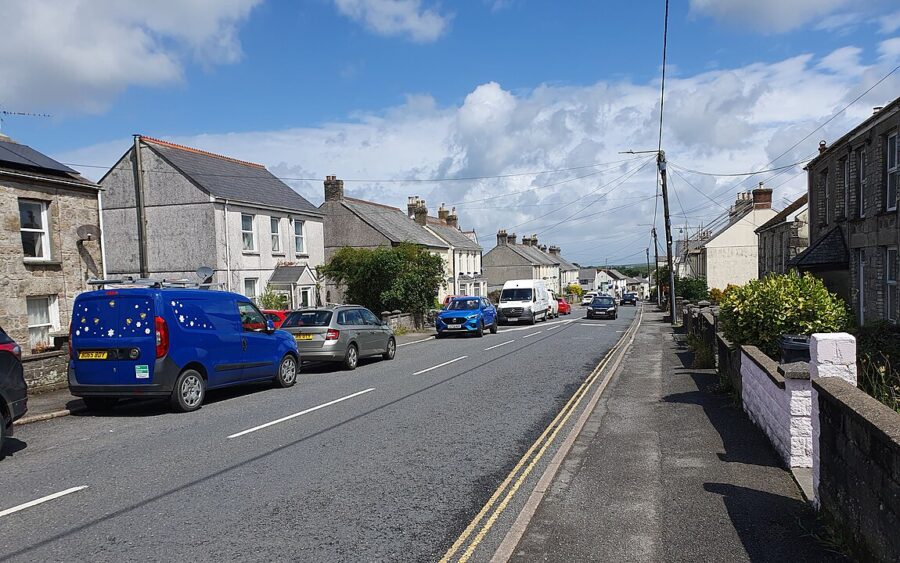 Fore Street in St Ives, Cornwall, showing a street lined with parked cars on either side.
