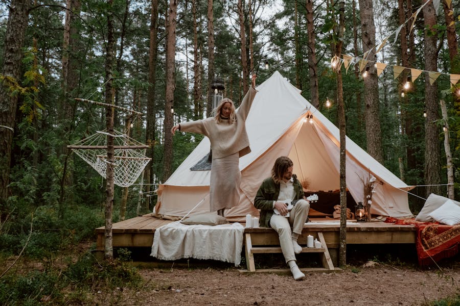 Serene forest glamping with tent, joyful couple, music, and cozy decor.