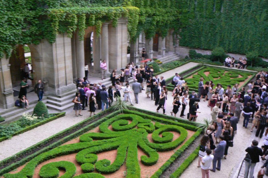 Formal courtyard parterre garden party with clipped hedges and stone arcade, historic Paris setting.