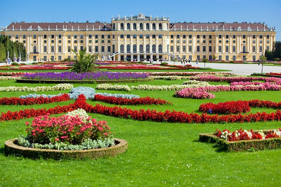 Schönbrunn Palace formal gardens in Vienna with colorful parterres and yellow palace façade.