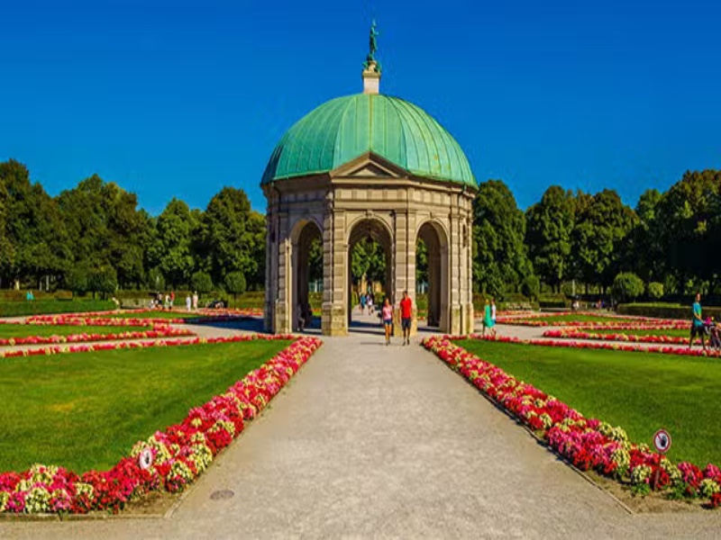 Hofgarten domed pavilion in formal garden with gravel path and colorful flowerbeds.