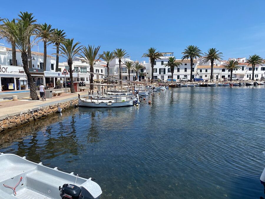 Boats are docked in a tranquil body of water in Fornells, Menorca, surrounded by scenic views.