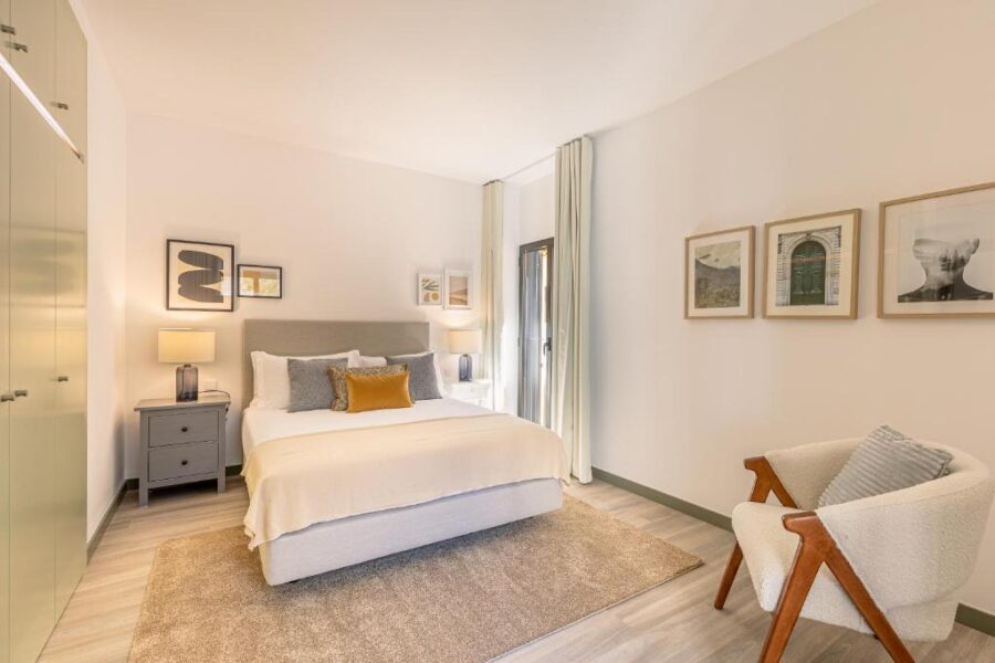 Interior of a bedroom at Fort Bay Suite Apartments, showcasing a bed, a chair, and decorative wall pictures.
