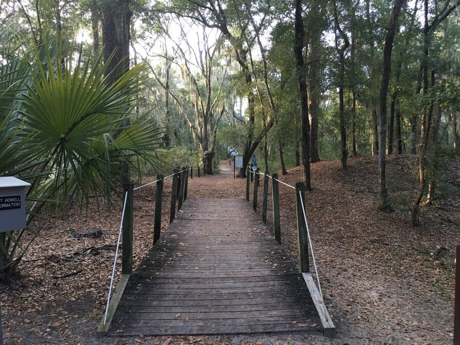Wooden bridge extends into a wooded trail at Fort Howell, Hilton Head Island, framed by trees and natural scenery.


