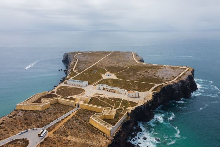 Aerial view of historical Sagres coastal fortification on rocky island with turquoise ocean backdrop.