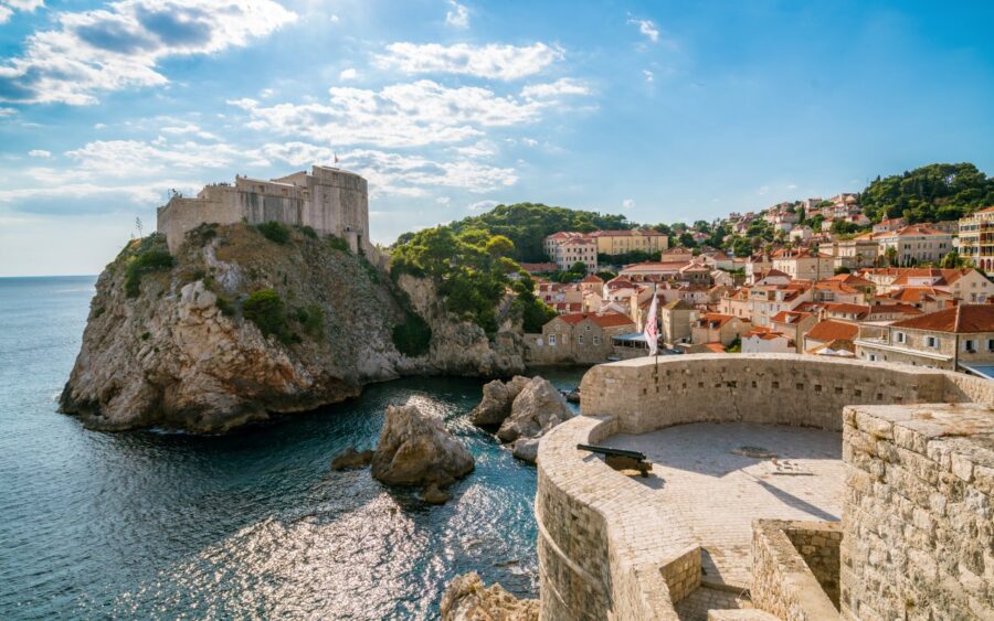Historic coastal fortress and Mediterranean village, scenic view with cannon and turquoise waters.