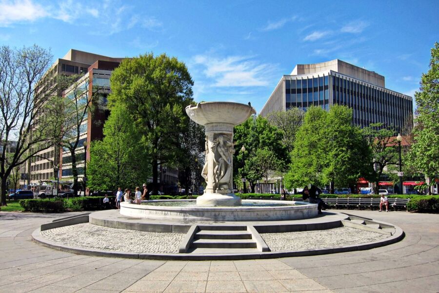 Fountain in DuPont Circle urban park surrounded by modern architecture, trees, and relaxing people.