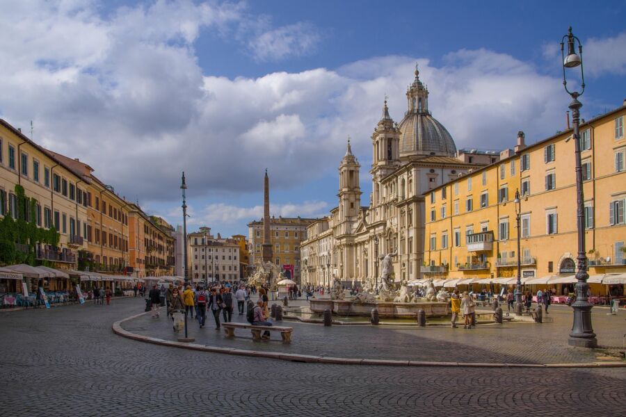 Historic Italian square with grand architecture, bustling crowd, and ornate fountain on a sunny day.