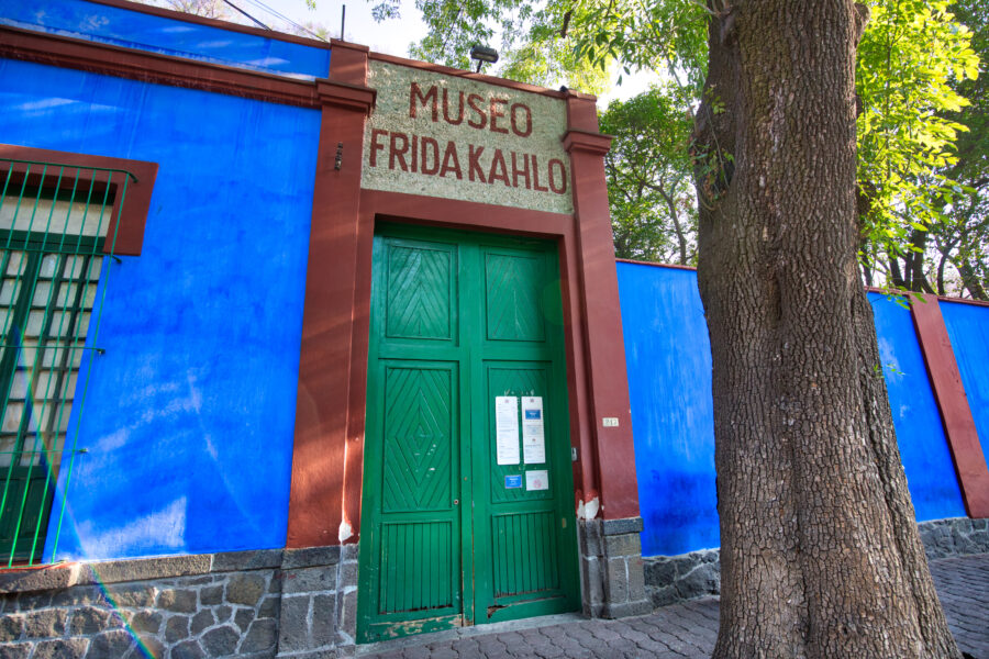 Front view of the Frida Kahlo Museum in Mexico, showcasing its vibrant blue exterior and lush greenery surrounding the entrance