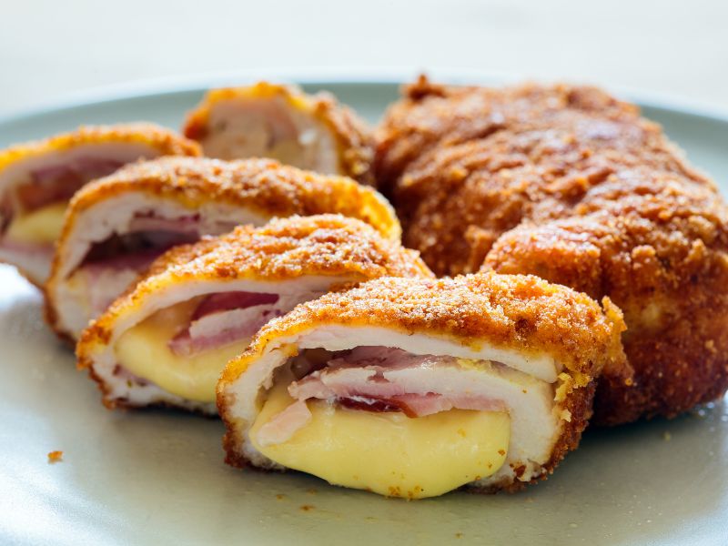 Golden-brown fried chicken stuffed with creamy cheese and ham on an elegant plate.