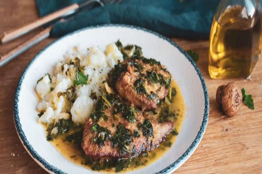 Pan-seared fish with herb sauce and mashed potatoes on rustic wooden table.