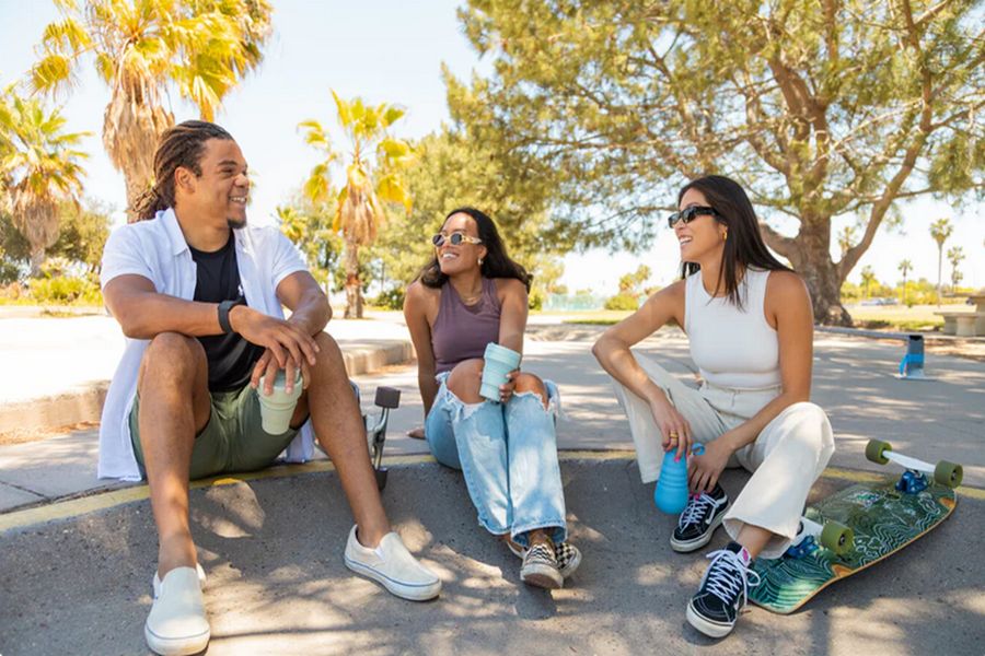 Friends enjoying sunny day in park with palm trees and skateboard.