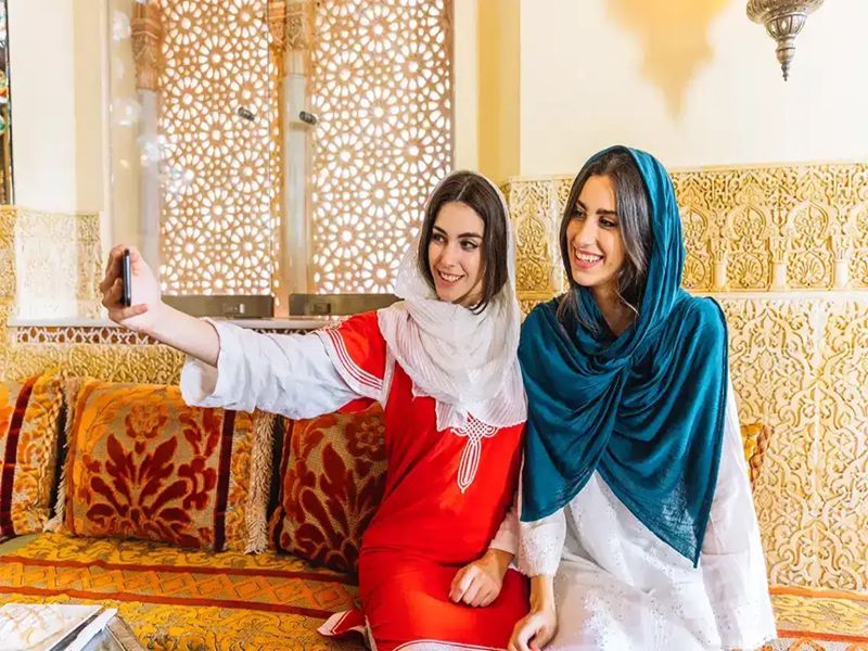Young women take a joyful selfie on a culturally rich patterned couch.