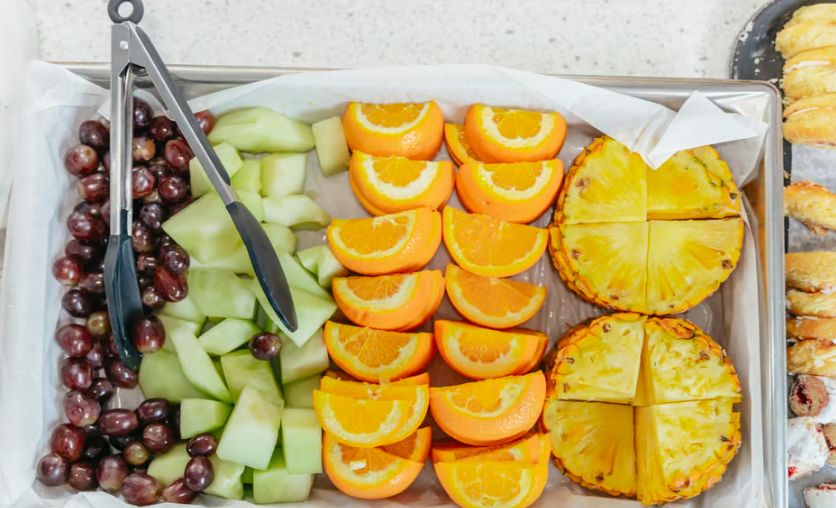 Fruit platter with grapes, honeydew, oranges, pineapple on parchment-lined tray.