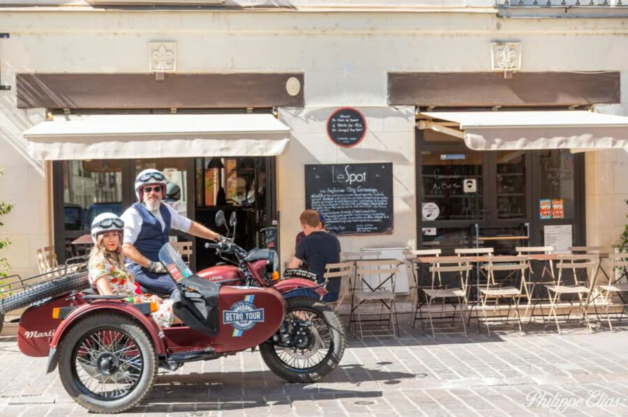 Man and child sit in a vintage sidecar motorcycle labeled "Retro Tour" outside a cafe called "Le Spot" in the Loire Valley.
