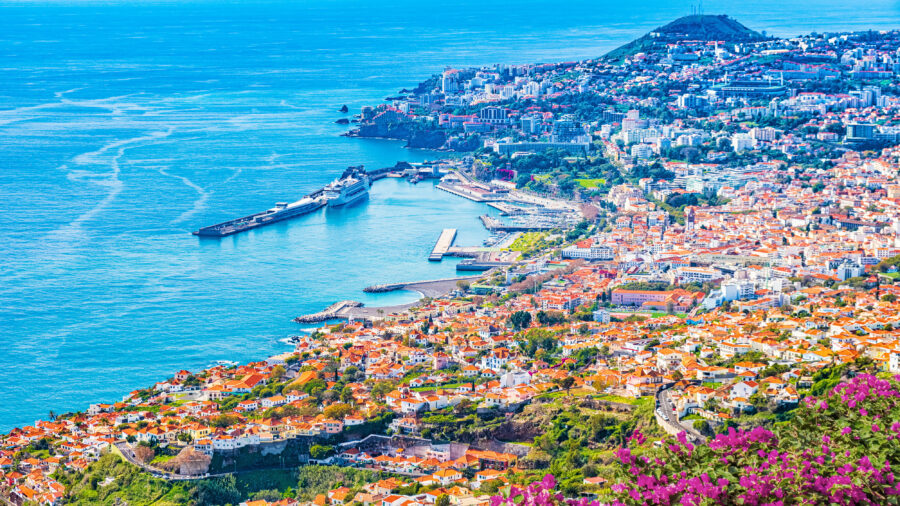 Panoramic view of Funchal, Madeira Island, showcasing vibrant buildings and lush hills against a clear blue sky.
