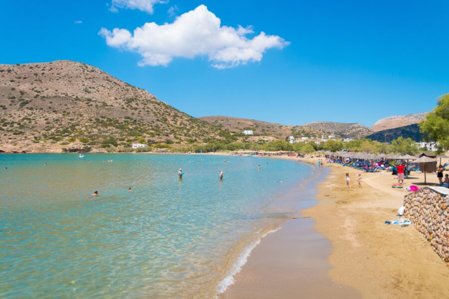 Galissas beach on Syros island, featuring golden sand and clear blue waters, surrounded by lush greenery and rocky hills.

