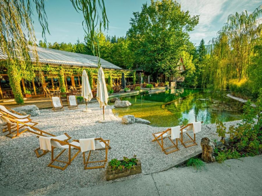 Garden scene at Garden Village Bled with chairs positioned beside a calm pond, framed by vibrant plants.