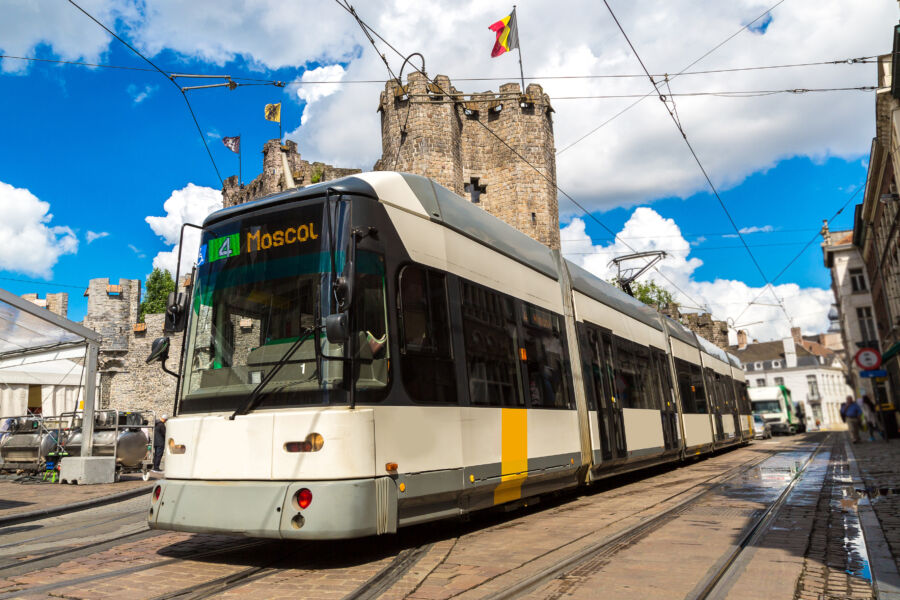 Bright summer day in Gent, Belgium, features a city tram moving along the street, framed by lush trees and charming buildings.