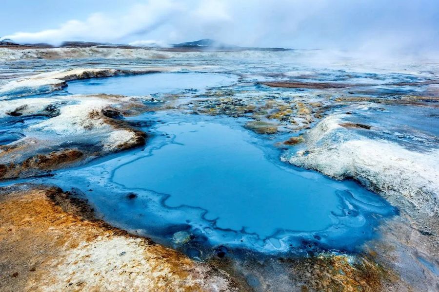 Geothermal landscape with vibrant blue pool, mineral deposits, and steaming hot springs.