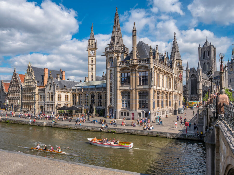People stroll along the Graslei promenade by the river Lys, showcasing medieval architecture and St Michael's Bridge in Ghent.