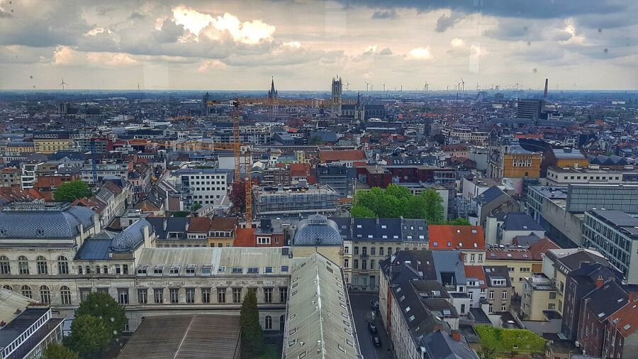 Panoramic view of Ghent's cityscape from a tower, showcasing historic buildings and waterways under a clear blue sky.