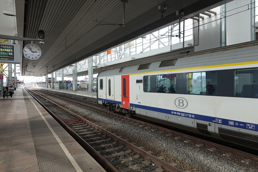 Train arrives at Ghent-Sint-Pieters Station, featuring a prominent clock displaying the time.