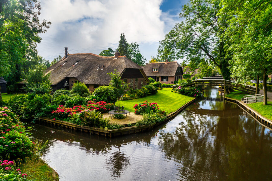 Giethoorn canal with thatched roof cottages, wooden footbridge and lush gardens.